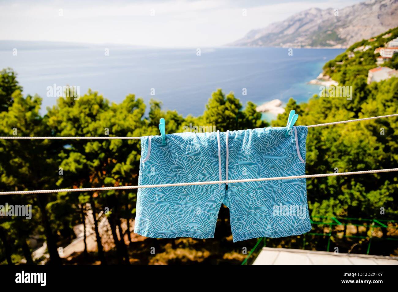 Short de bain bleu pour hommes accroché à la corde à linge du fond marin Banque D'Images Short de bain bleu pour hommes accroché à la corde à linge du fond marin Banque D'Images