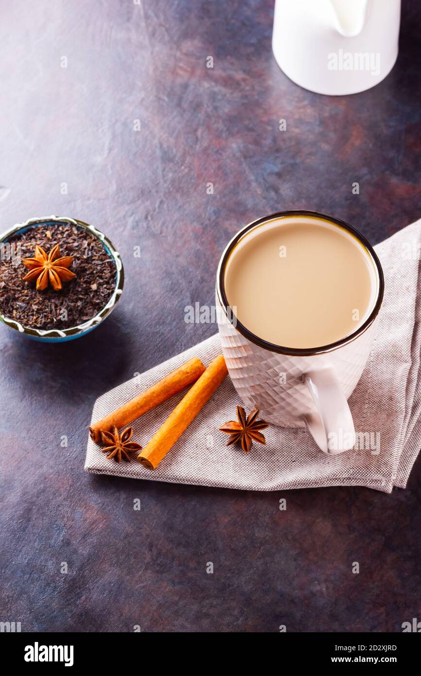 Thé Chai de masala. Boisson traditionnelle indienne - thé masala avec épices sur fond sombre. Tasse d'épices en céramique, thé et pot à lait blanc Banque D'Images