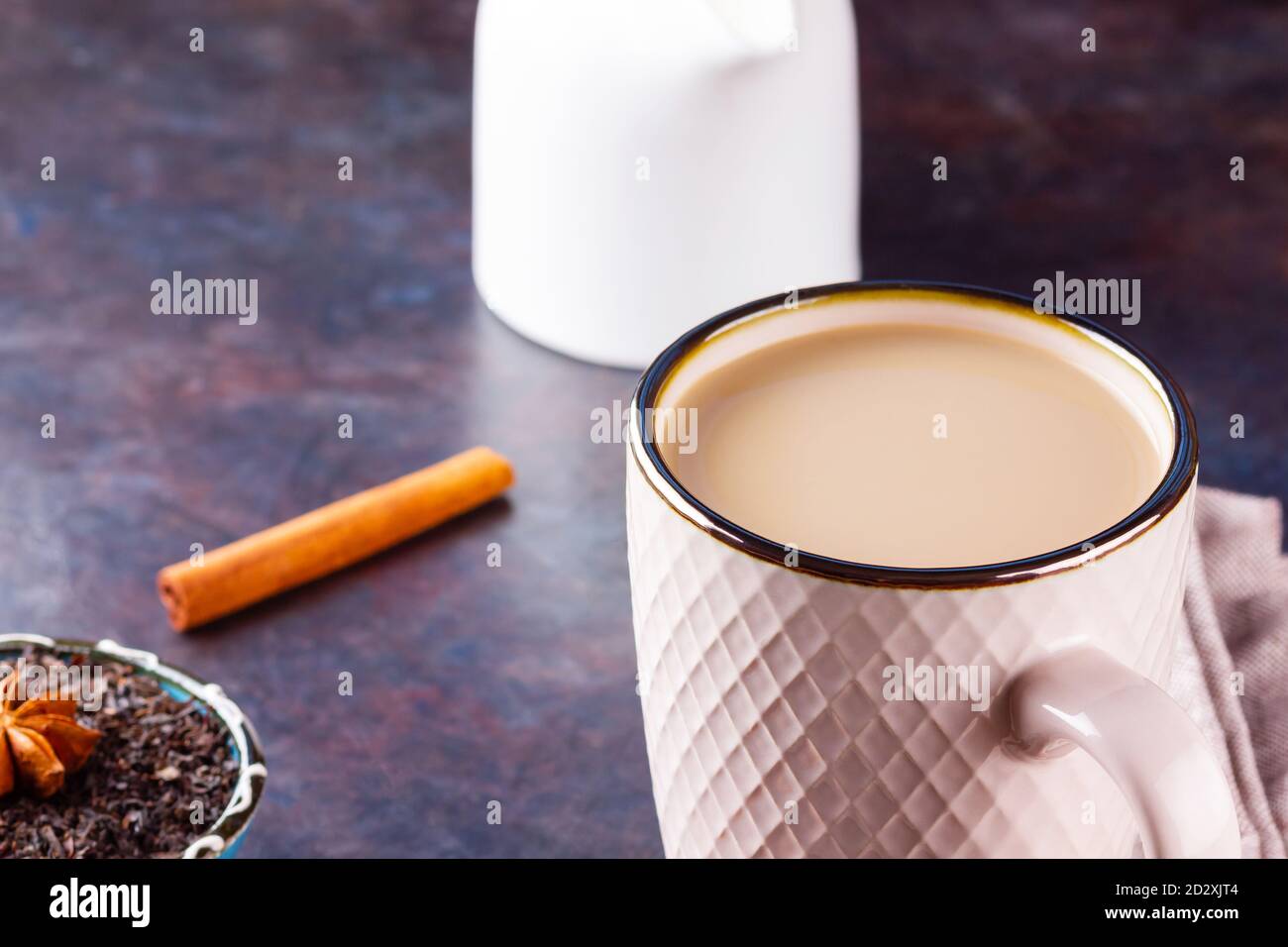 Thé Chai de masala. Boisson traditionnelle indienne - thé masala avec épices sur fond sombre. Tasse d'épices en céramique, thé et pot à lait blanc Banque D'Images