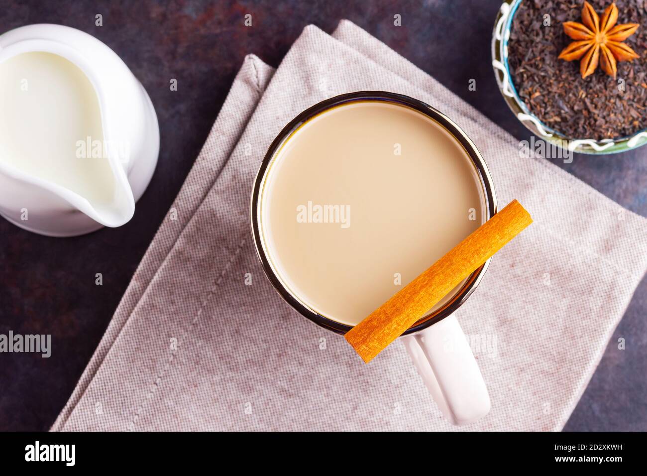 Thé Chai de masala. Boisson traditionnelle indienne - thé masala avec épices sur fond sombre. Tasse d'épices en céramique, thé et pot à lait blanc Banque D'Images