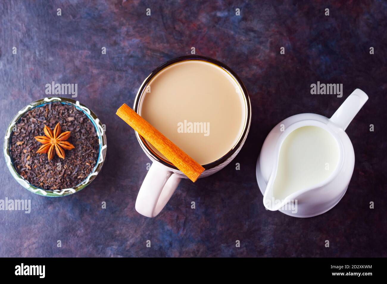 Thé Chai de masala. Boisson traditionnelle indienne - thé masala avec épices sur fond sombre. Tasse d'épices en céramique, thé et pot à lait blanc Banque D'Images