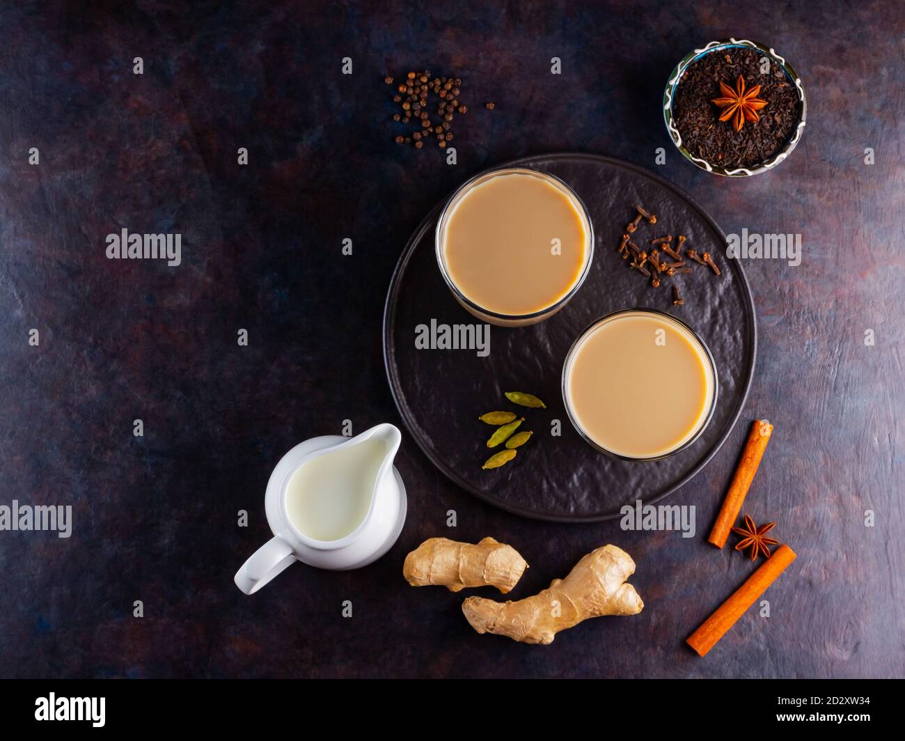Thé Chai de masala. Boisson traditionnelle indienne - thé masala avec diverses épices sur une assiette noire. Deux verres transparents avec thé masala sur un dos noir Banque D'Images