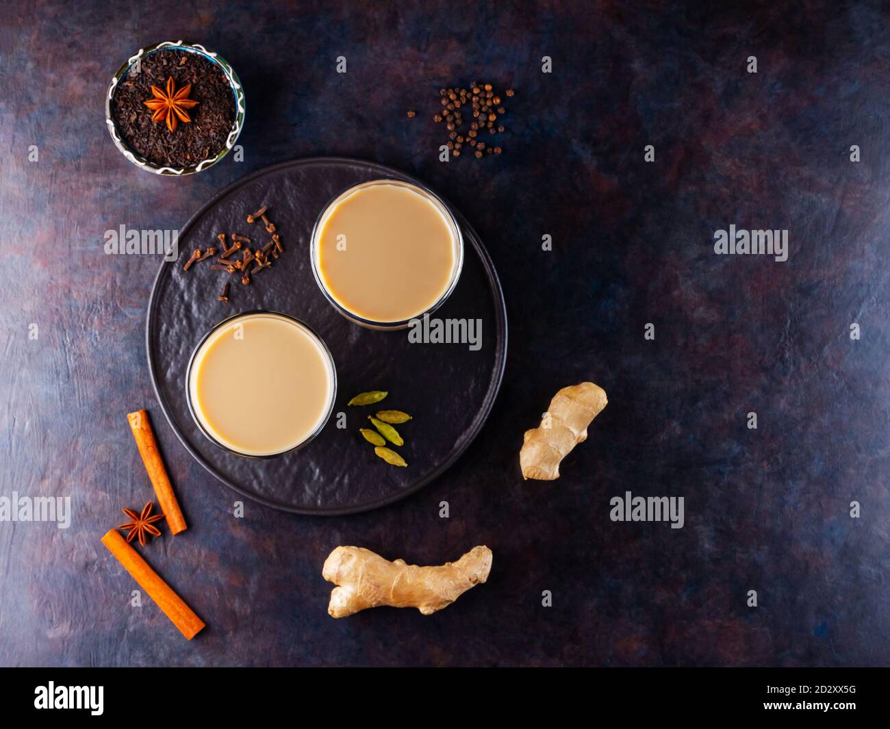Thé Chai de masala. Boisson traditionnelle indienne - thé masala avec diverses épices sur une assiette noire. Deux verres transparents avec thé masala sur un dos noir Banque D'Images