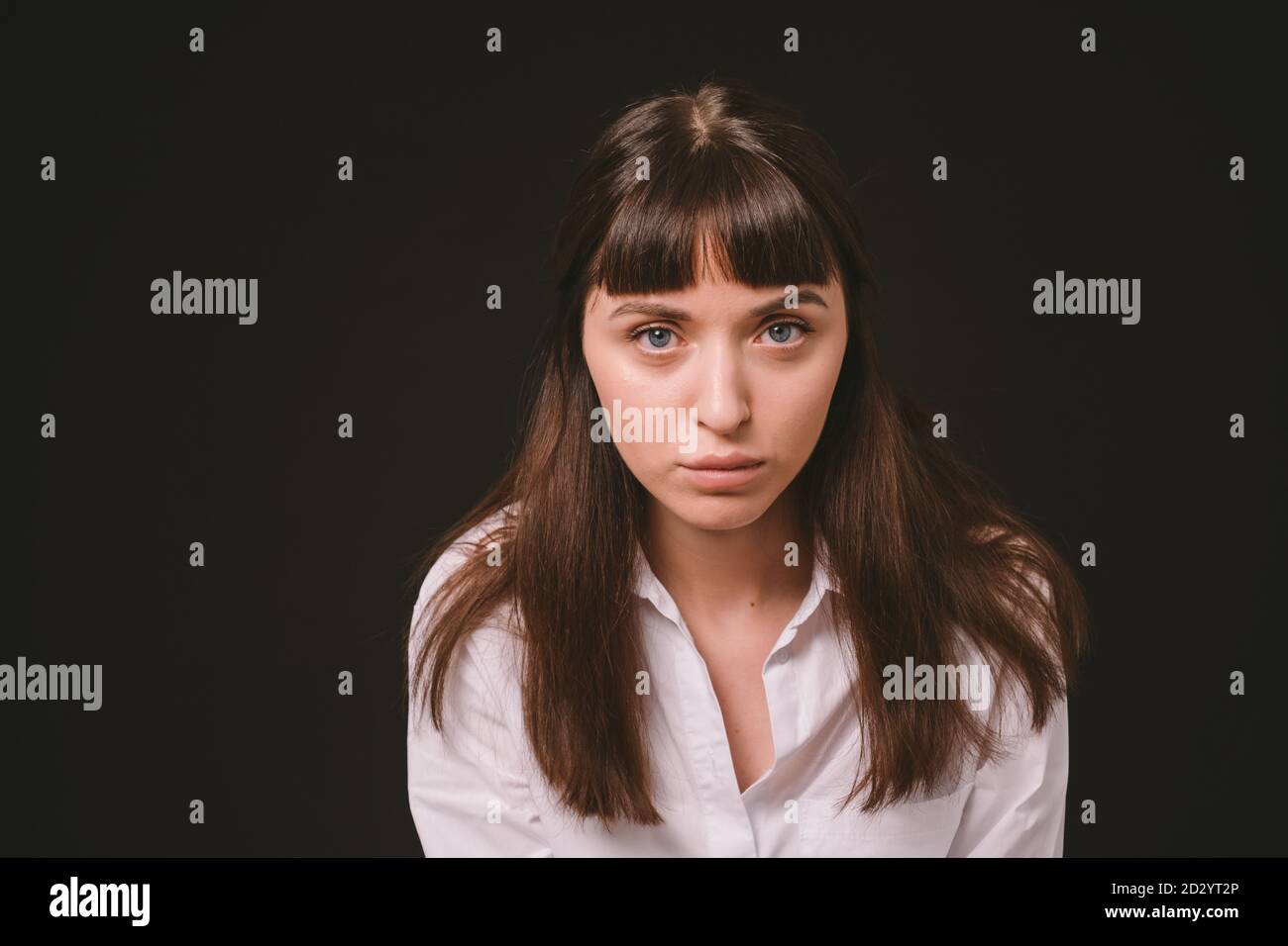 Portrait studio d'une jolie femme brune dans une chemise blanche, sur fond noir Uni, regardant sérieusement l'appareil photo Banque D'Images