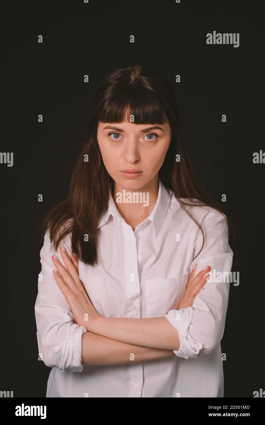 Portrait studio d'une jolie femme brune dans une chemise blanche sur fond noir Uni, regardant l'appareil photo Banque D'Images