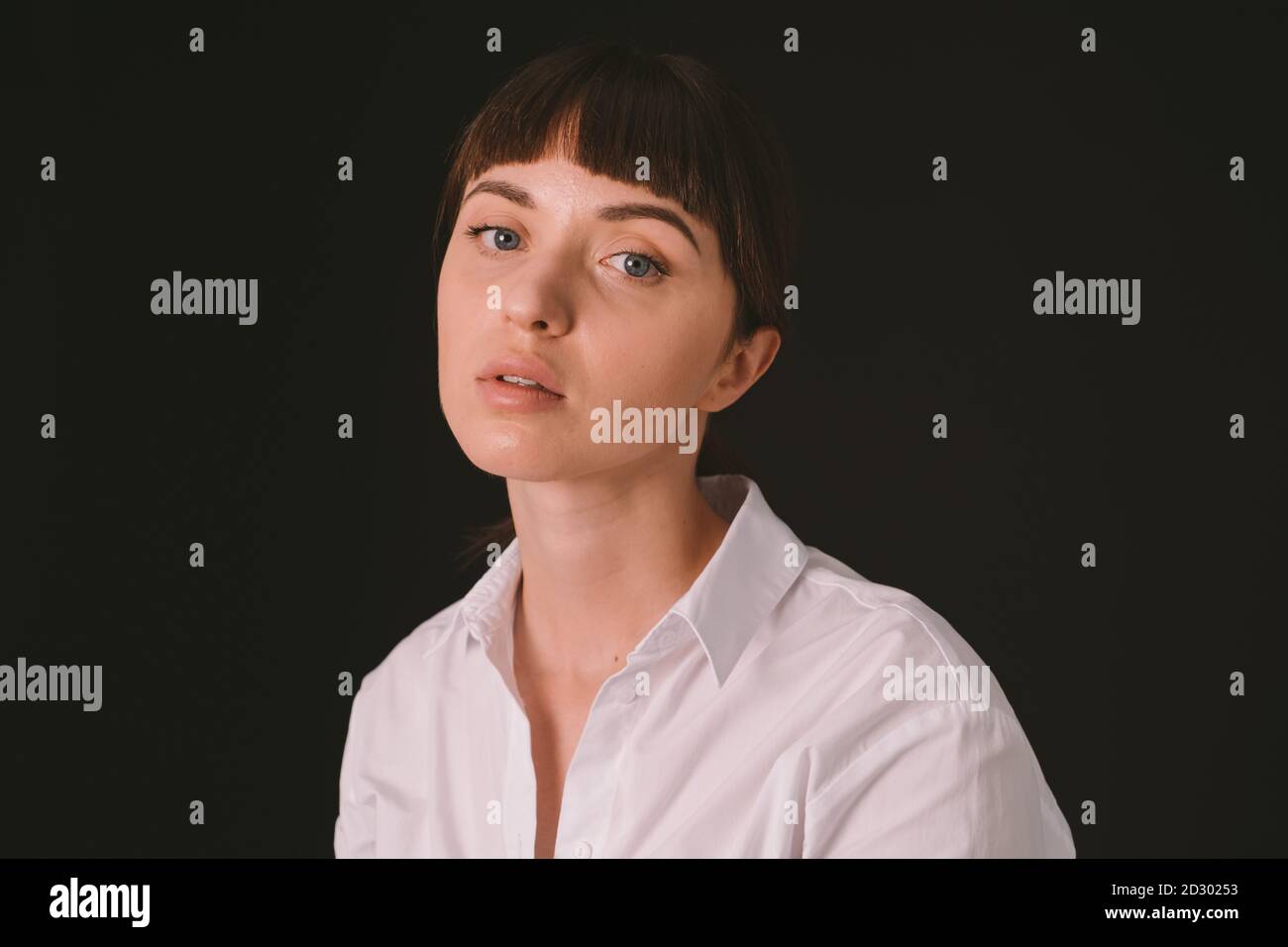 Portrait studio d'une jolie femme brune dans une chemise blanche sur fond noir Uni, regardant l'appareil photo Banque D'Images