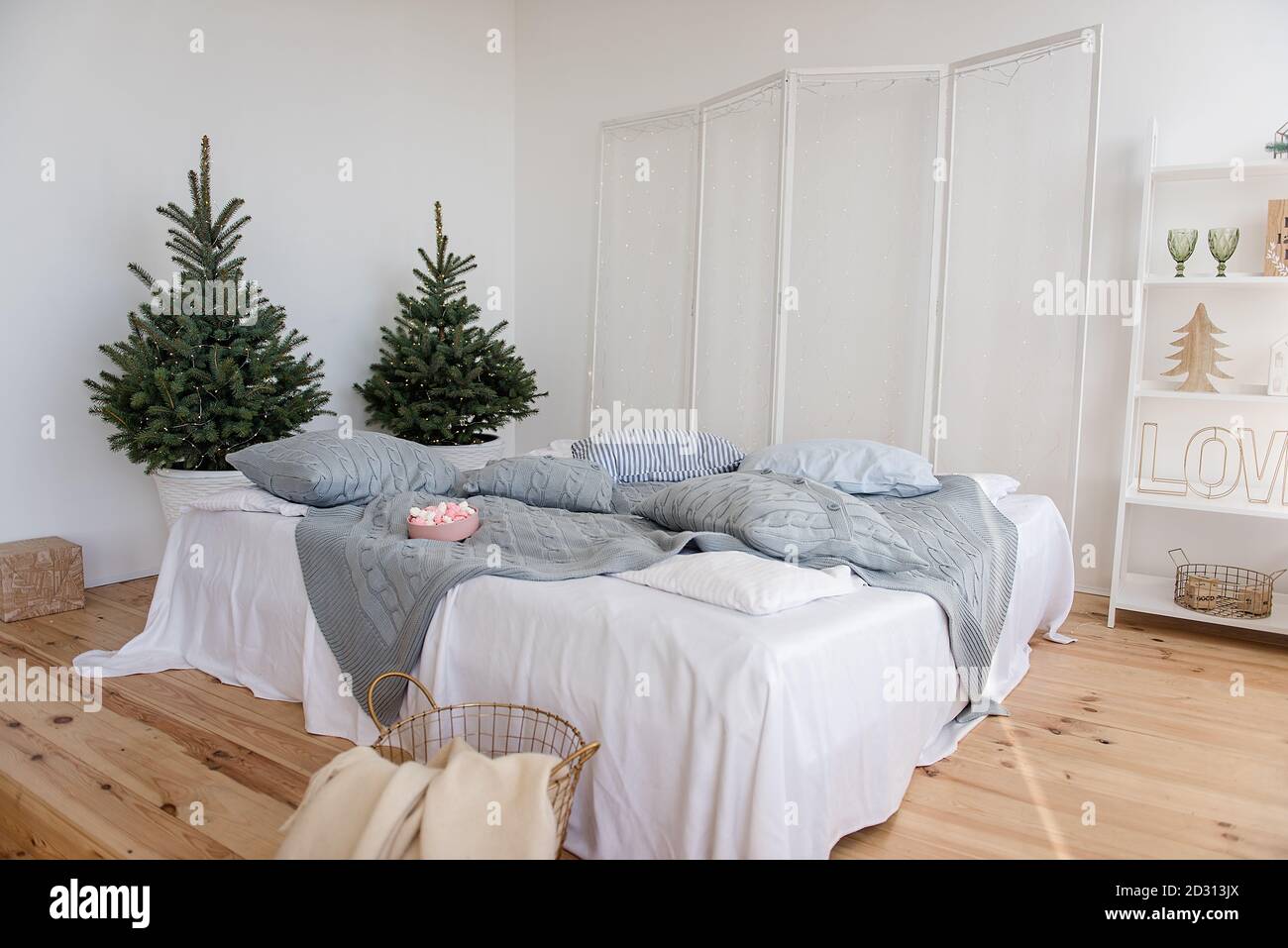 Chambre blanche élégante, minimalisme, style scandinave. Draps blancs, tissu écossais gris tricoté, oreillers. Parquet. Il y a des arbres de Noël avec guirlande Banque D'Images