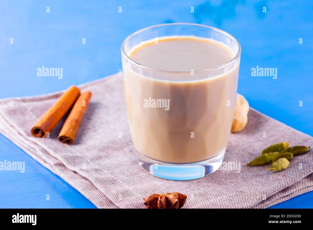 Thé au chaï masala sur une serviette en lin. Boisson traditionnelle indienne - thé masala avec diverses épices. Verre de thé masala sur fond bleu Banque D'Images