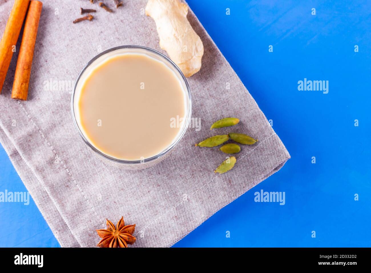 Thé au chaï masala sur une serviette en lin. Boisson traditionnelle indienne - thé masala avec diverses épices. Verre de thé masala sur fond bleu Banque D'Images