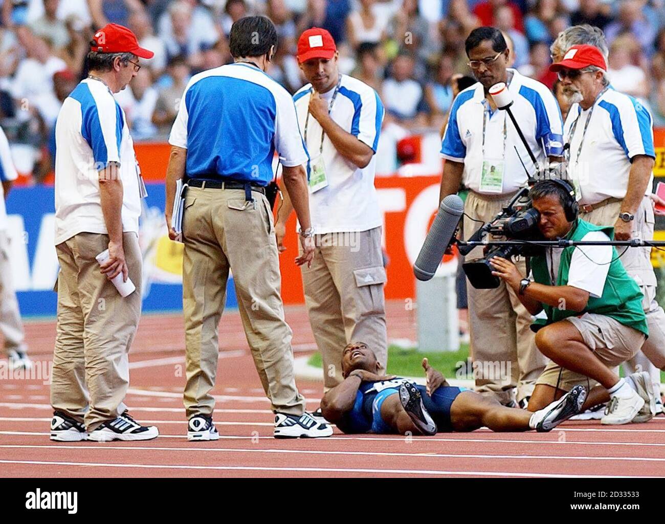 Les officiels entourent Jon Drummond (en bas) des États-Unis alors qu'il se trouve sur le dos, refusant de sortir de la piste après qu'il ait été disqualifié dans le quart-finale du 100m masculin aux Championnats du monde d'athlétisme à Paris, en France, le dimanche 24 août 2003. Banque D'Images