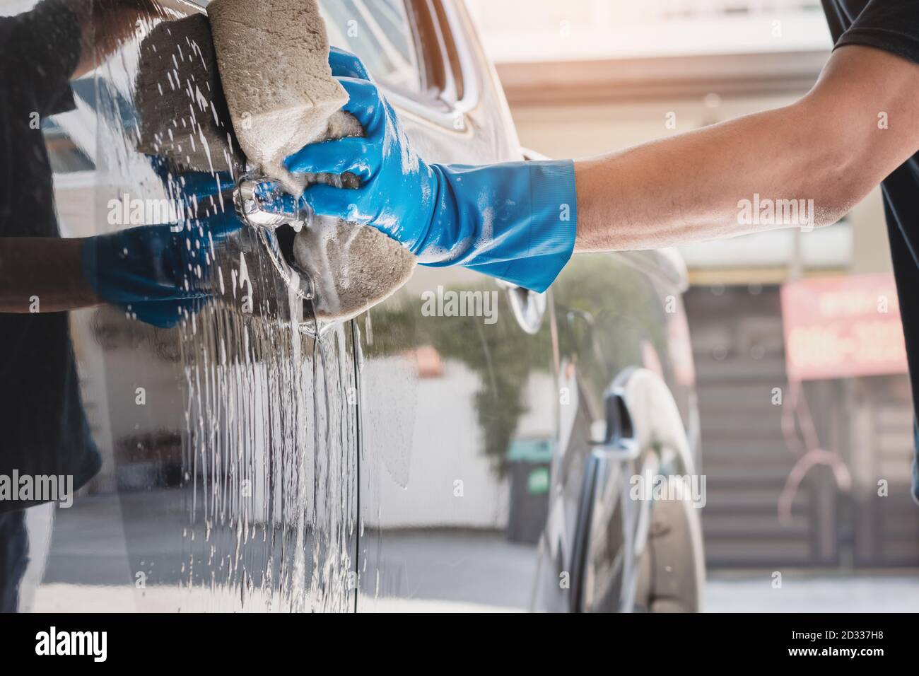 Personnel de lavage de voiture portant des gants en caoutchouc bleu à l'aide d'une éponge humidifiée avec du savon et de l'eau pour nettoyer la voiture. Banque D'Images