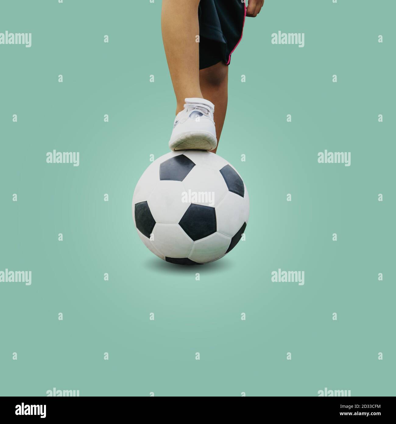 Gros plan pieds d'un garçon portant des baskets blanches marcher sur une balle de football isolée sur fond pastel, avec un chemin d'écrêtage. Banque D'Images