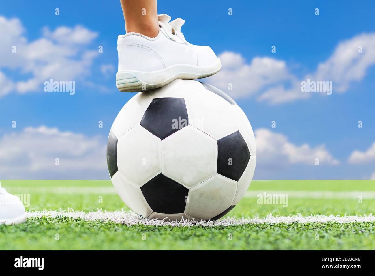 Pieds d'un garçon portant des baskets blanches qui marche sur une balle de football au milieu du terrain de football. Banque D'Images