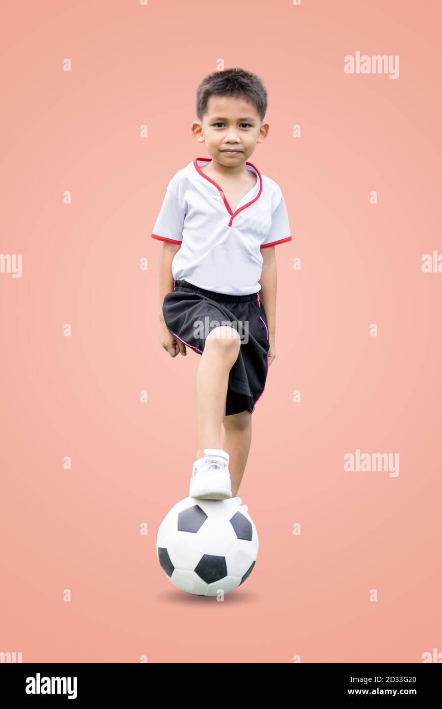 Le garçon portant des baskets de sport est en marche sur une balle de football isolée sur fond pastel, avec un chemin de coupure. Banque D'Images