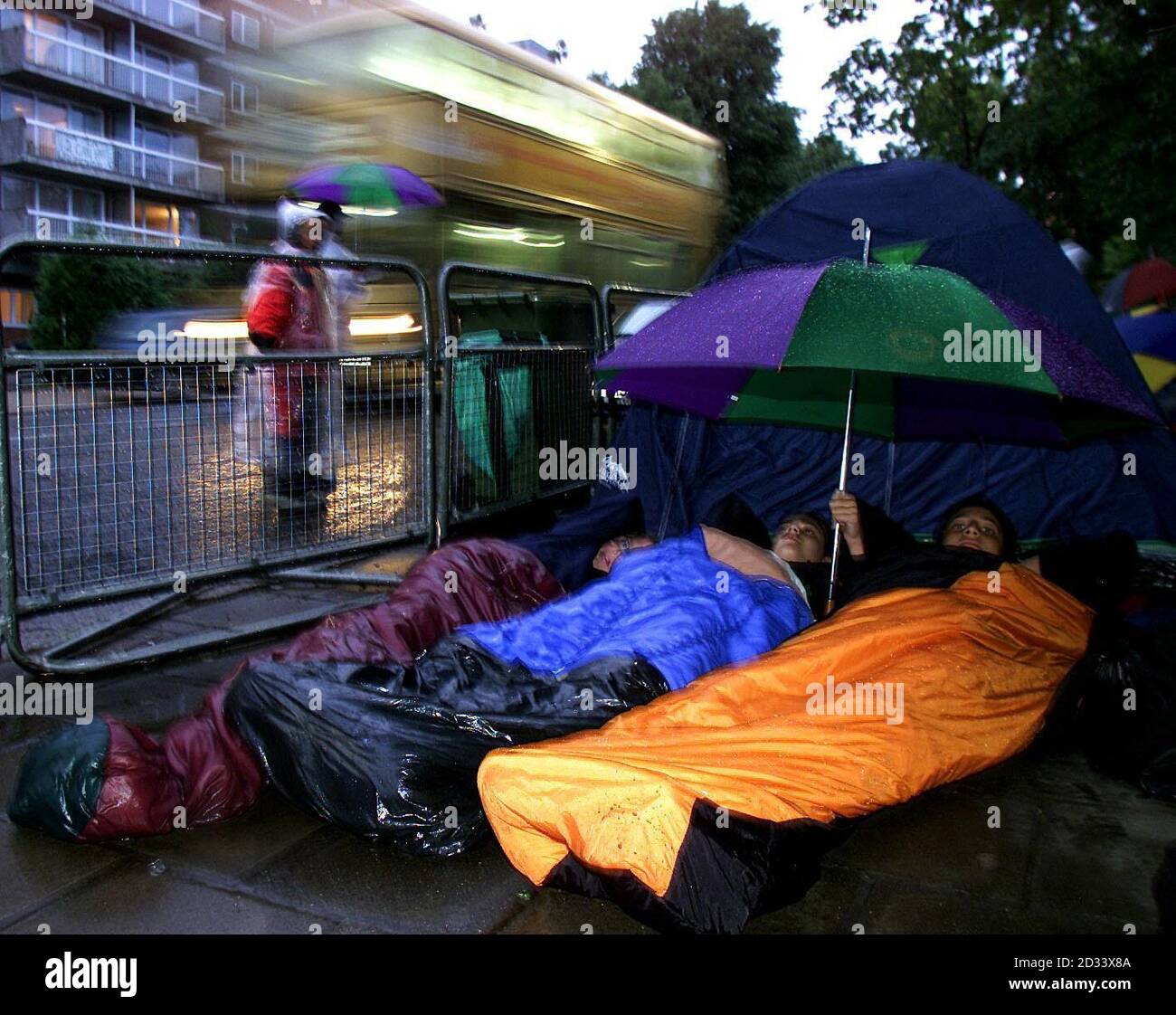 Misha Crosby (au centre) avec ses amis James Lewis (à gauche) et Omar Tantawy se préparent à dormir la nuit sous la pluie avec seulement un parapluie à couvrir à l'extérieur du championnat de tennis de Wimbledon dans l'espoir de voir Tim Henman en Grande-Bretagne jouer son sixième quart de finale de Wimbledon en sept ans lorsqu'il prend la route Le brésilien insemé Andre sa. Banque D'Images