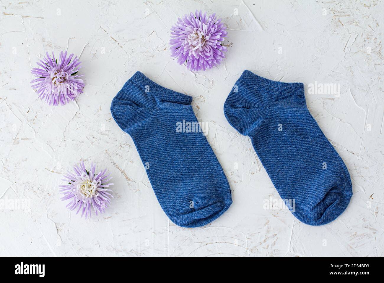 Paire de chaussettes et de fleurs d'aster pour femmes sur fond blanc structuré, vue du dessus. Banque D'Images