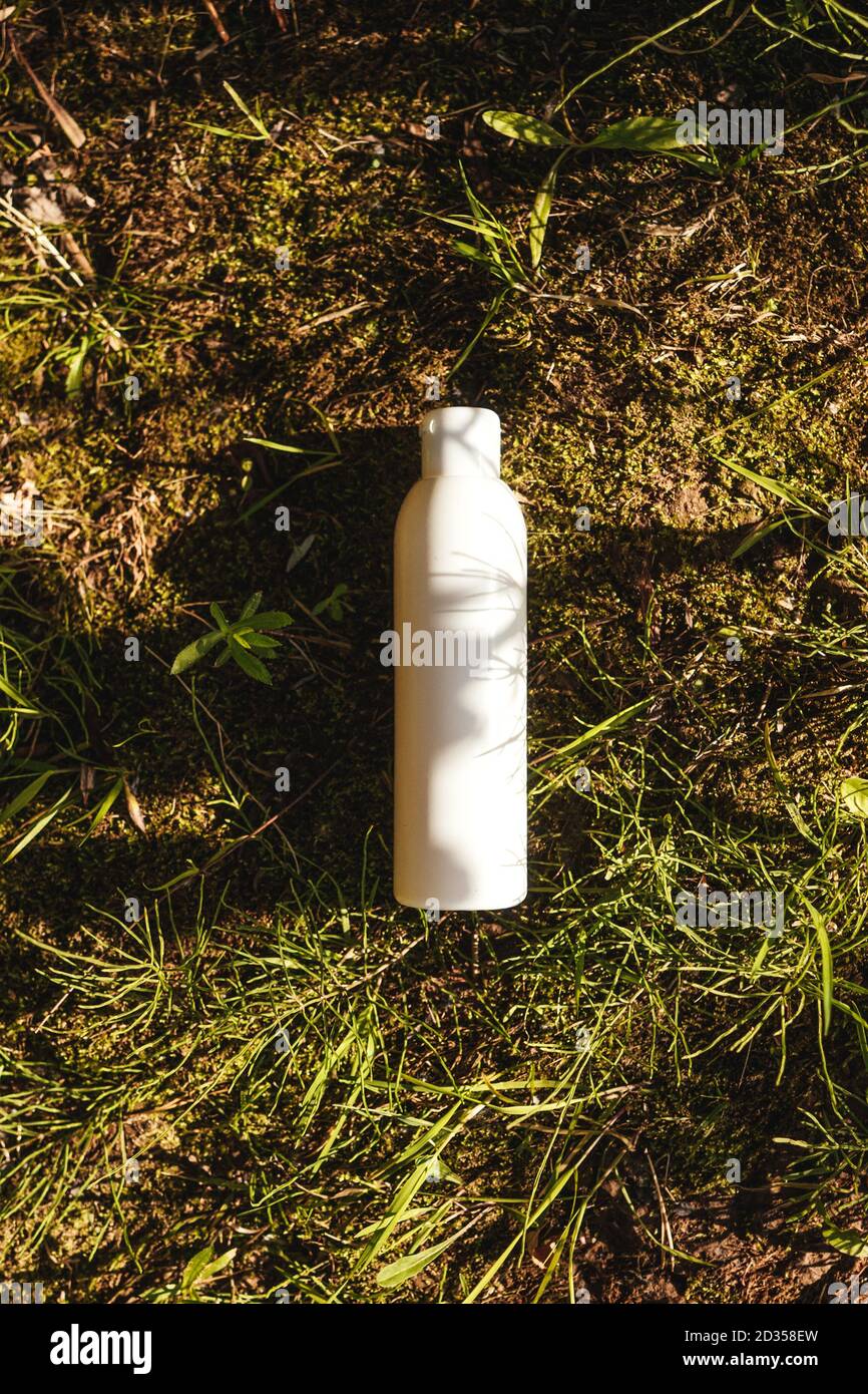 Bouteille blanche sur fond vert-marron naturel. Cosmétique ou bouteille d'eau, concept écologique. Herbe, mousse, terre. Banque D'Images
