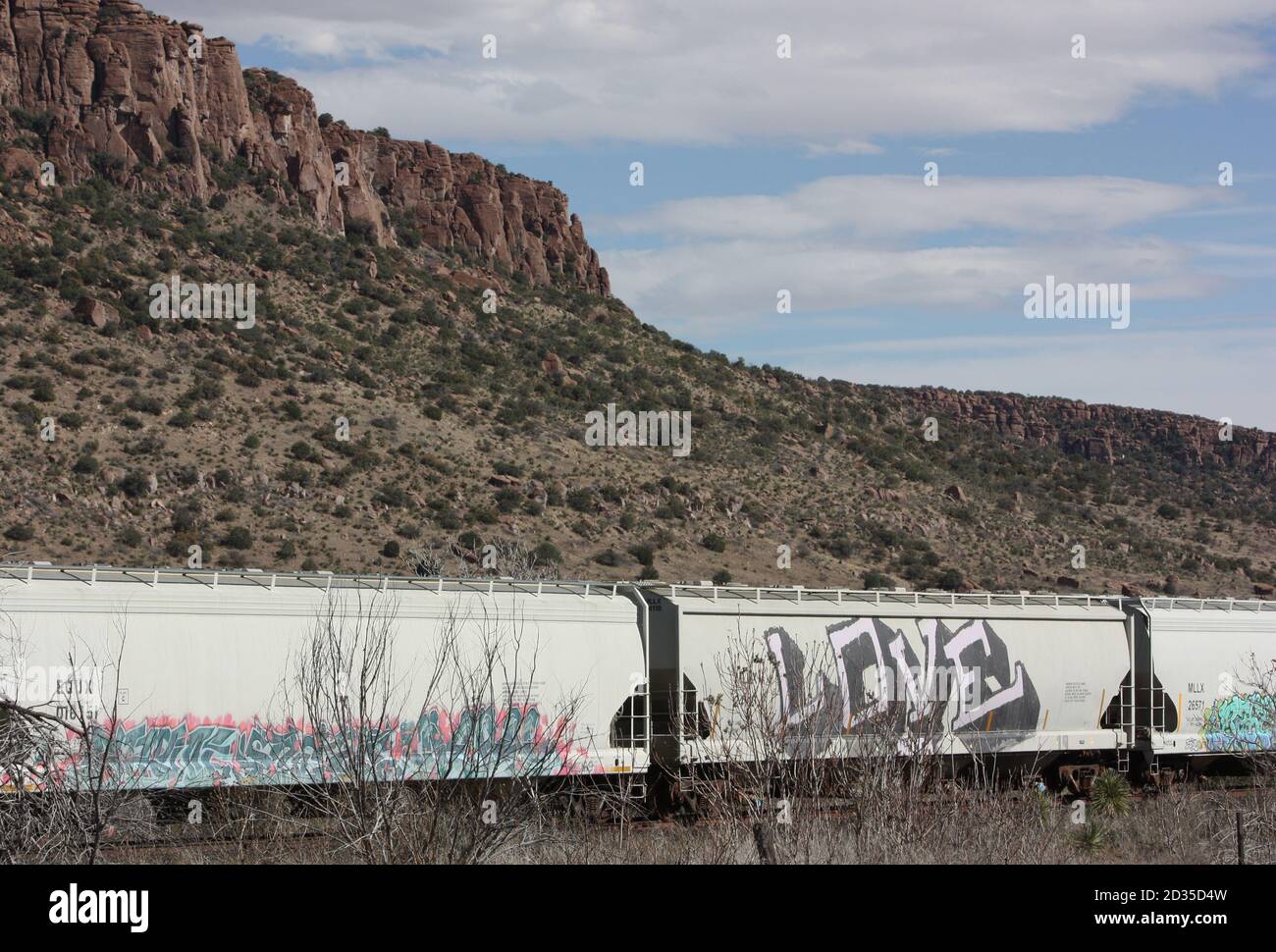 Voitures de chemin de fer Graffitied du train d'amour alignées l'horizon contre le rocher rouge butte sous ciel bleu clair Banque D'Images