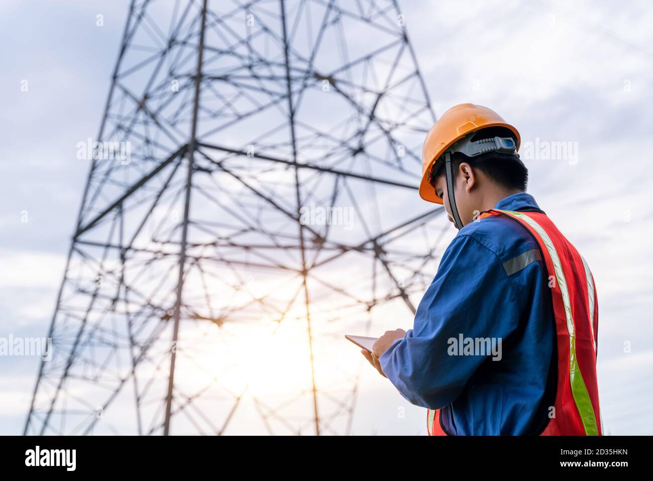 Les ingénieurs portent des vêtements de sécurité travaillant sur la tour haute tension, vérifier les informations sur le taplet. Banque D'Images