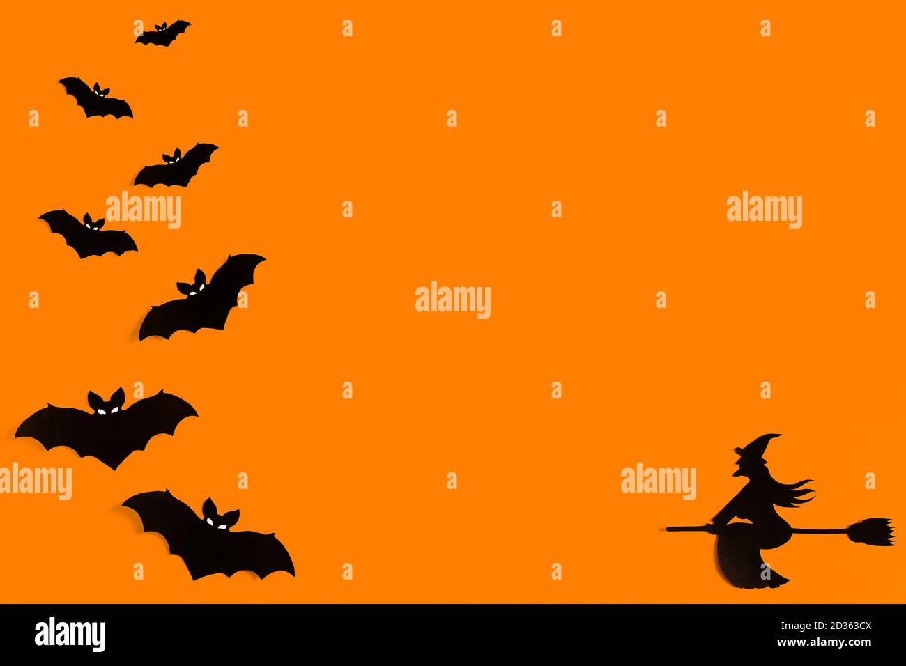 Silhouettes d'un troupeau de chauves-souris et d'une sorcière volant sur un balai en papier noir sur fond orange. Modèle de message d'accueil pour Halloween avec espace de copie Banque D'Images