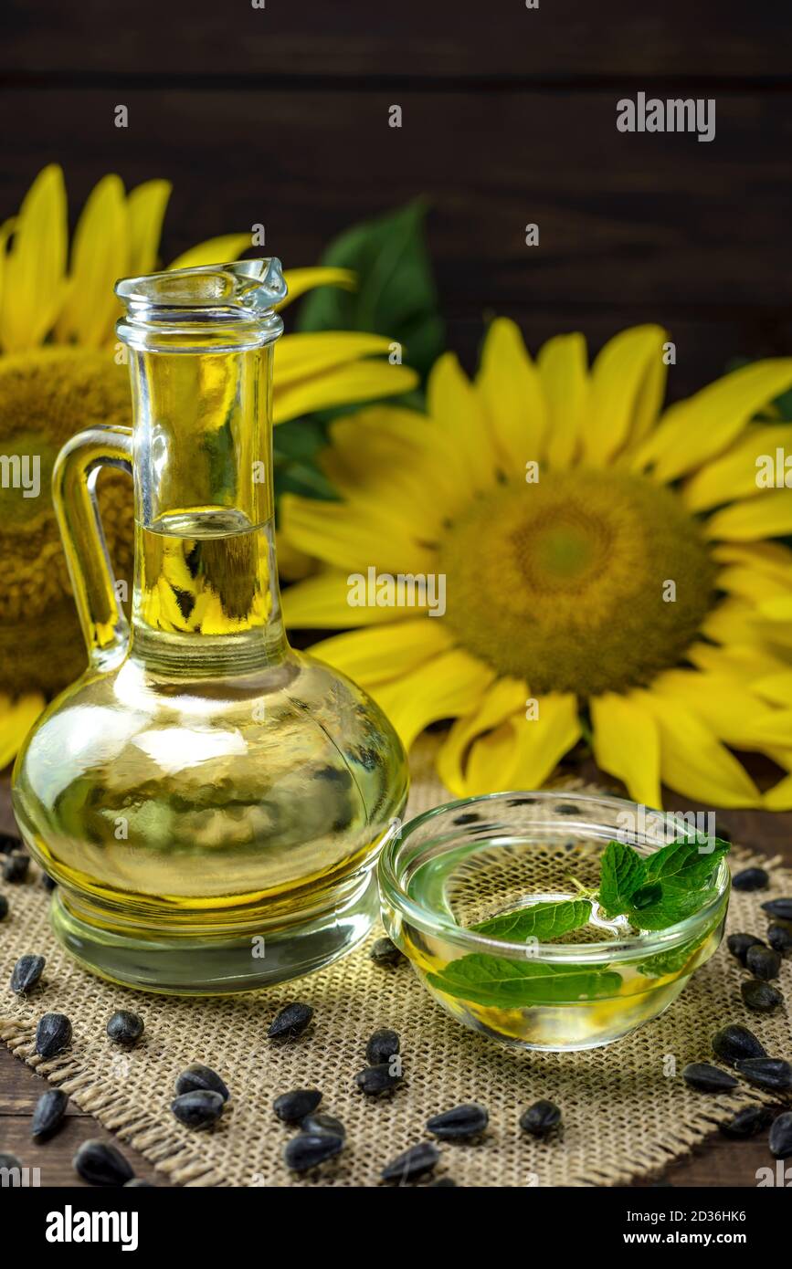 Huile de tournesol dans une bouteille et graines de tournesol près d'une fleur de tournesol fraîche sur fond de bois. Banque D'Images