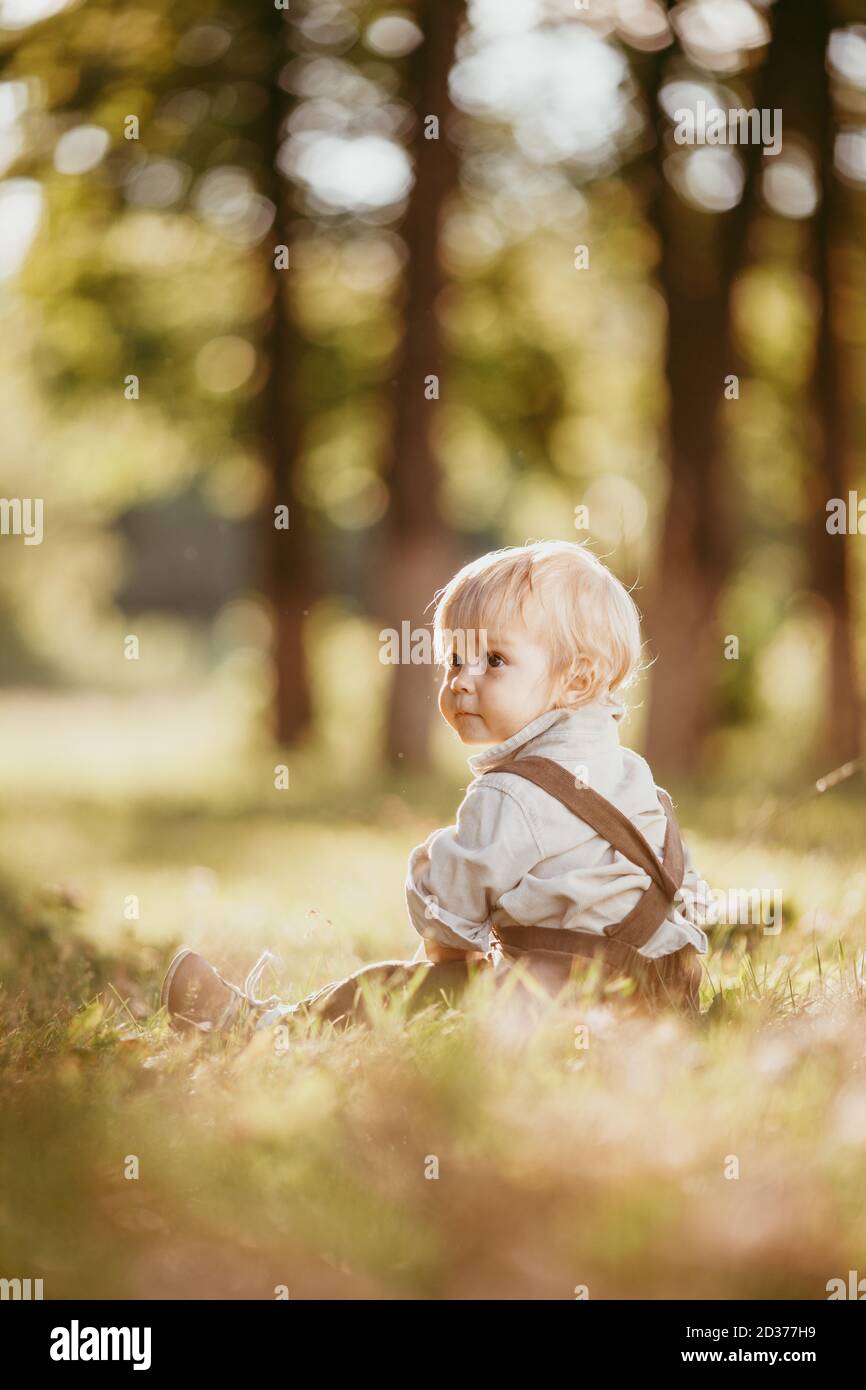 Un petit garçon blond vêtu d'une combinaison vintage un champ au coucher du soleil Banque D'Images