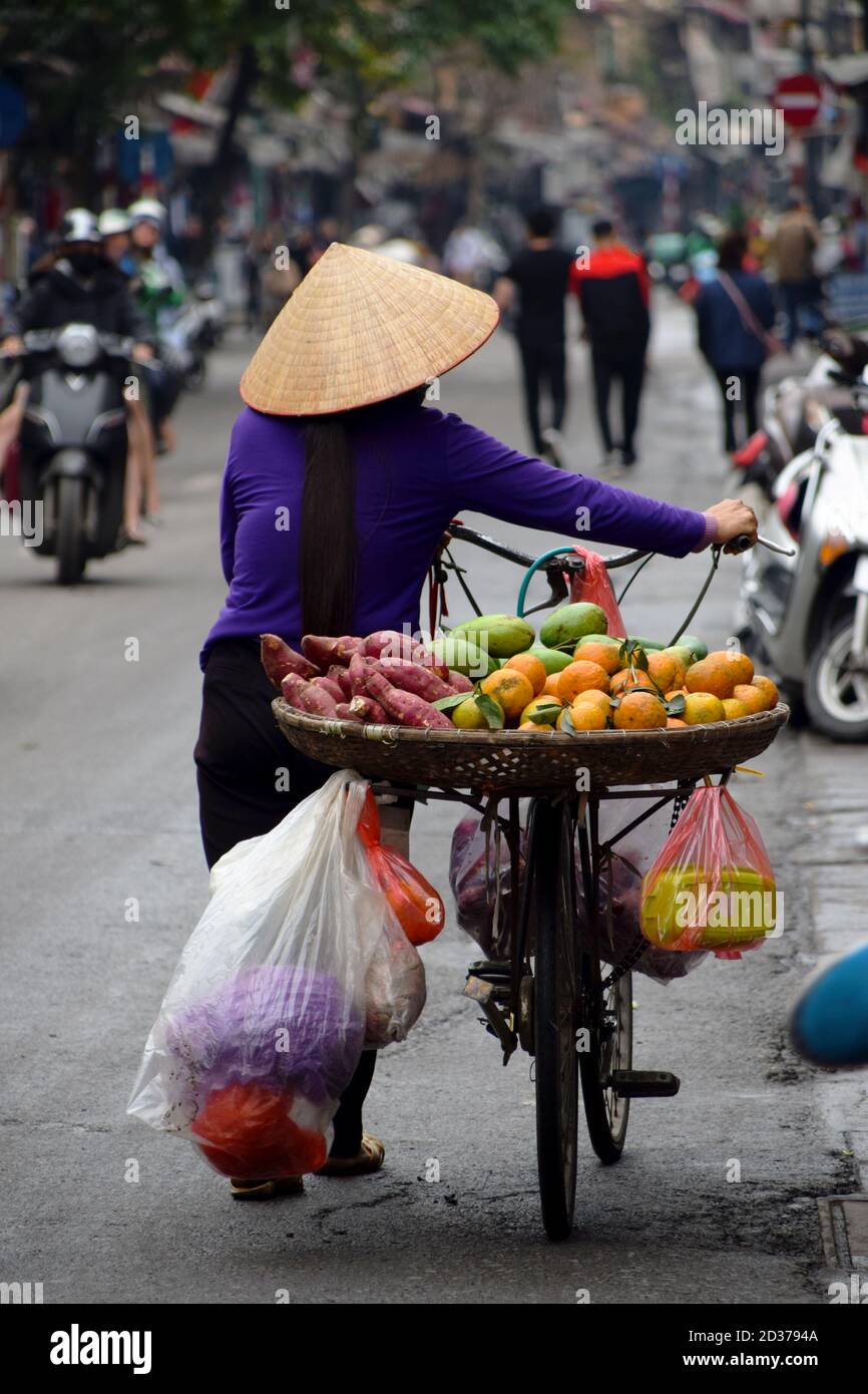 Femme vietnamienne et vendeur de rue marchant avec son vélo, dont elle vend des fruits et des légumes, dans les rues des vieux quartiers de Hanoi Banque D'Images