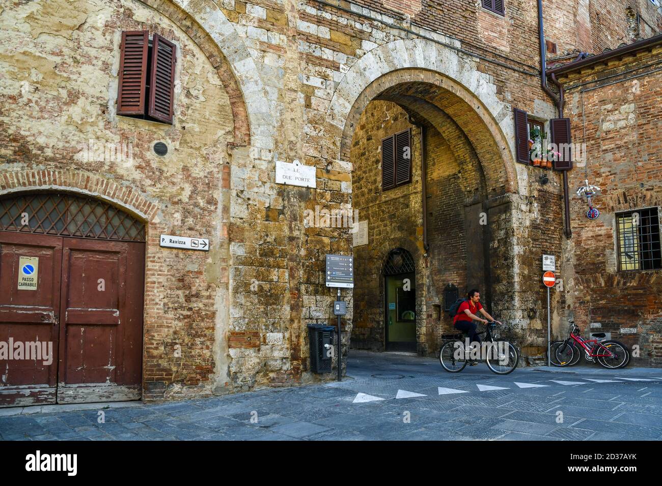 L'Arco delle due porte, porte médiévale du centre historique de Sienne, site classé au patrimoine mondial de l'UNESCO, avec un homme à vélo, Toscane, Italie Banque D'Images