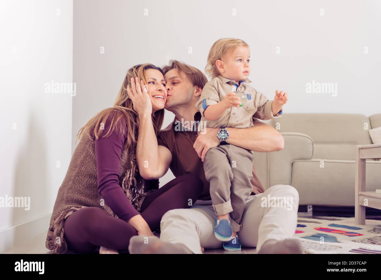 Famille heureuse assise sur le sol avec leur petit bébé. La famille passe du temps à la maison avec son fils. Père embrassant une mère. Banque D'Images