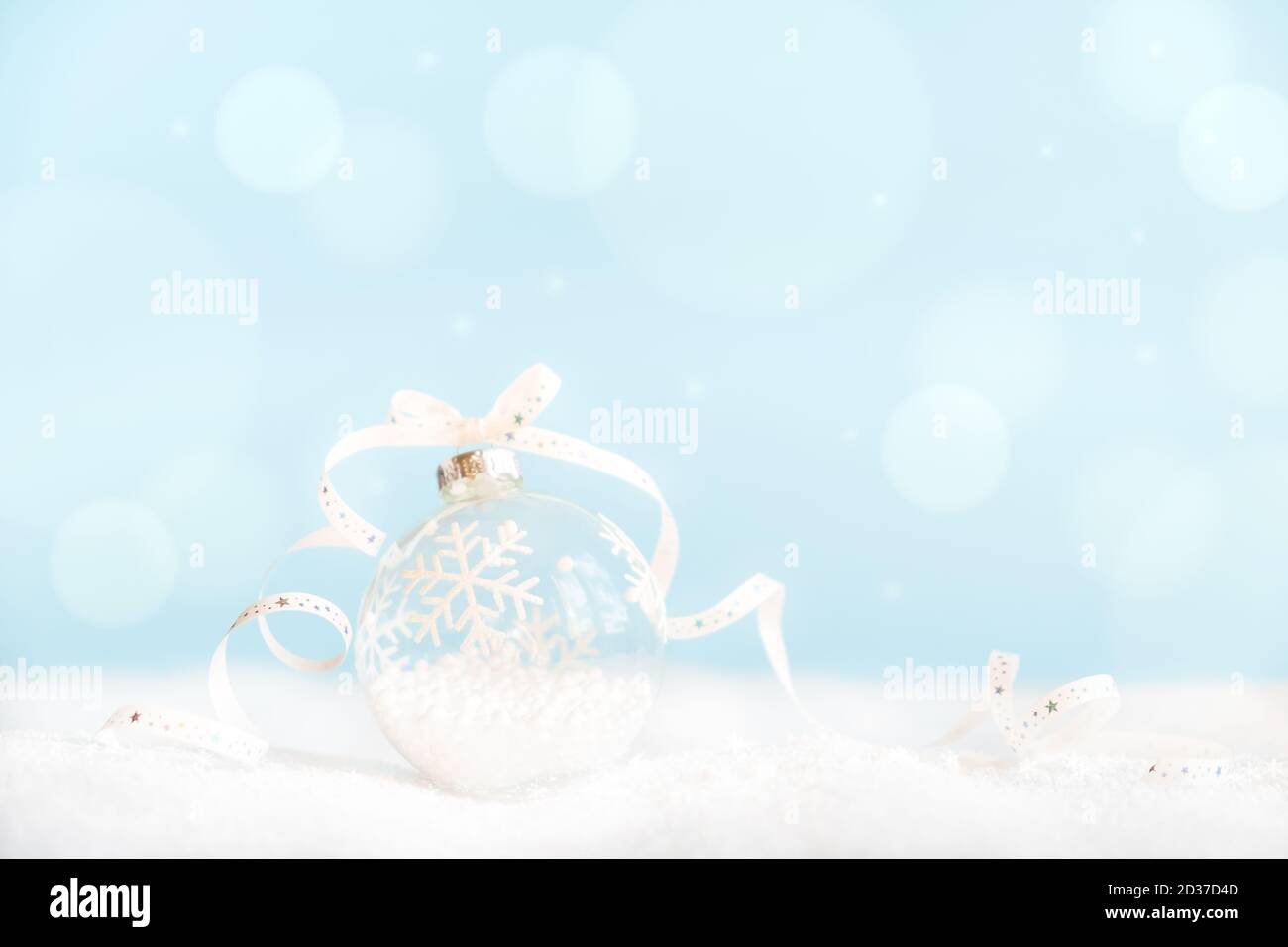 Boule de Noël avec ruban sur la surface avec neige et lumières défocacées avec espace de copie. Banque D'Images