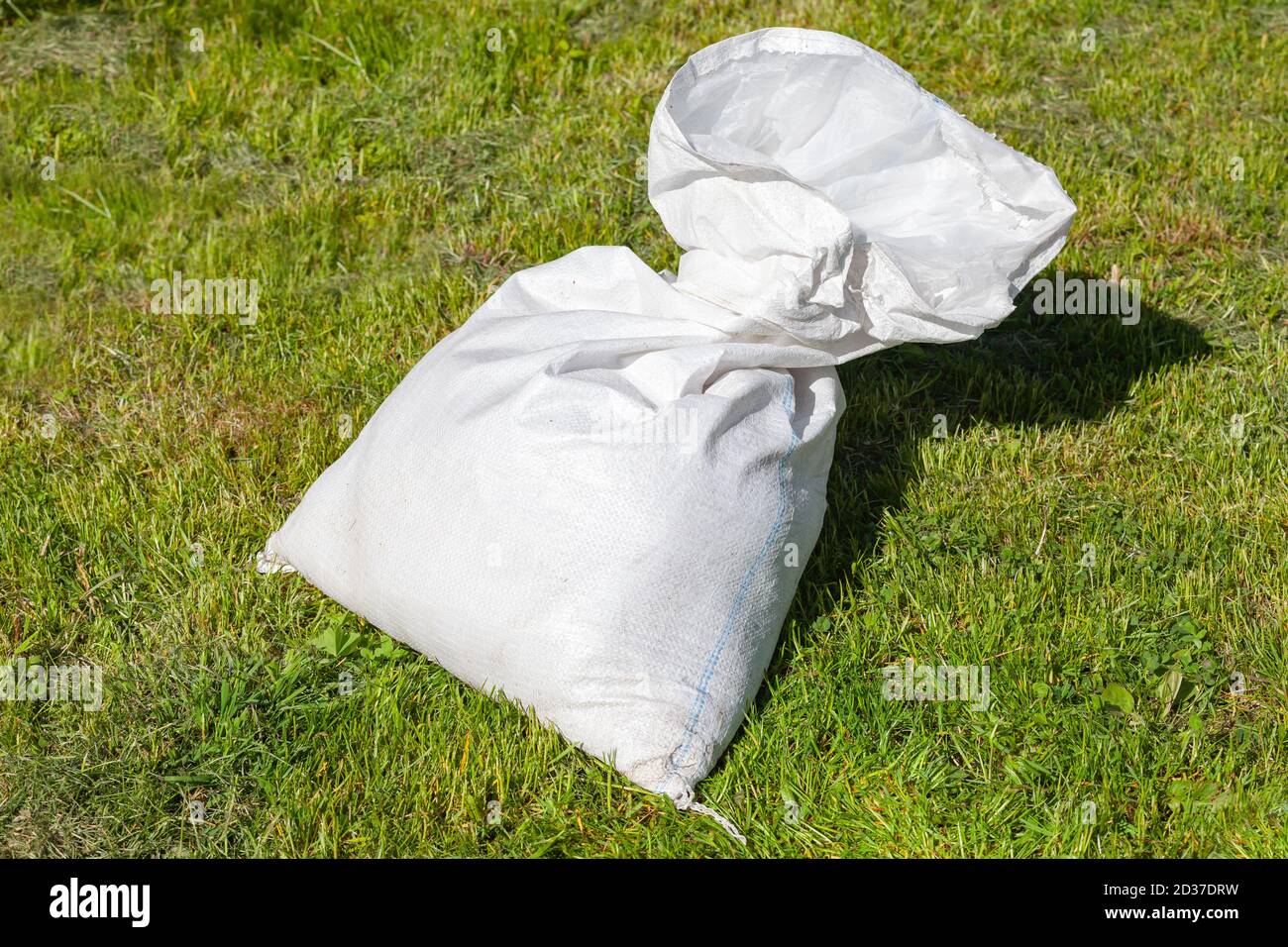 Le sac en polypropylène blanc à moitié vide repose sur l'herbe verte à jour ensoleillé Banque D'Images