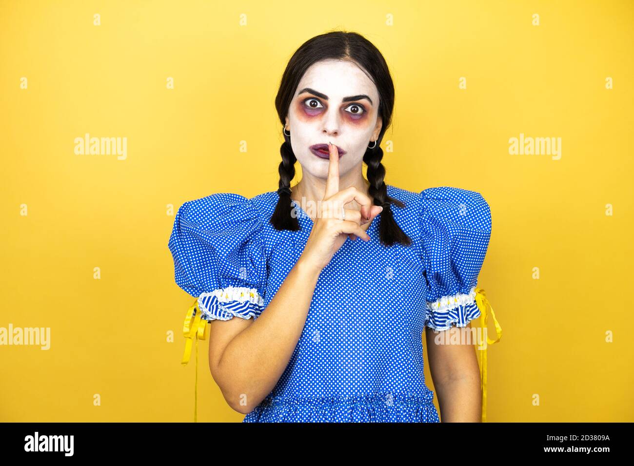 femme portant une poupée effrayante costume d'halloween sur fond jaune demandant à être calme avec le doigt sur les lèvres. Silence et concept secret. Banque D'Images