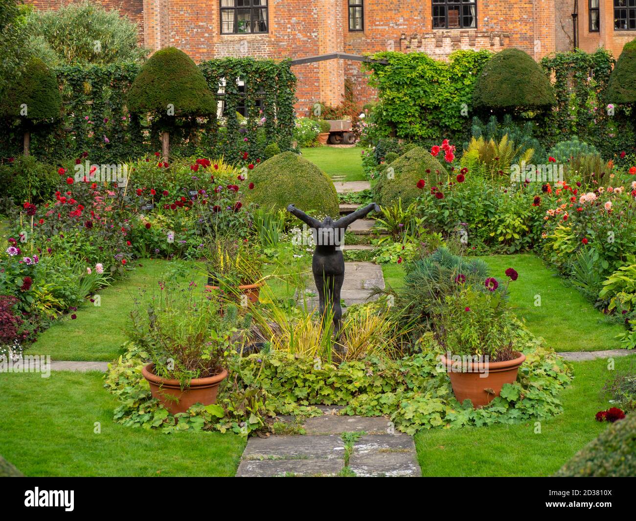 Chenies Manor House au soleil ; le jardin en contrebas en septembre avec la sculpture d'Alan Bigg sur « le plongeur », qui se retrouve à travers l'exposition dynamique des dahlia. Banque D'Images