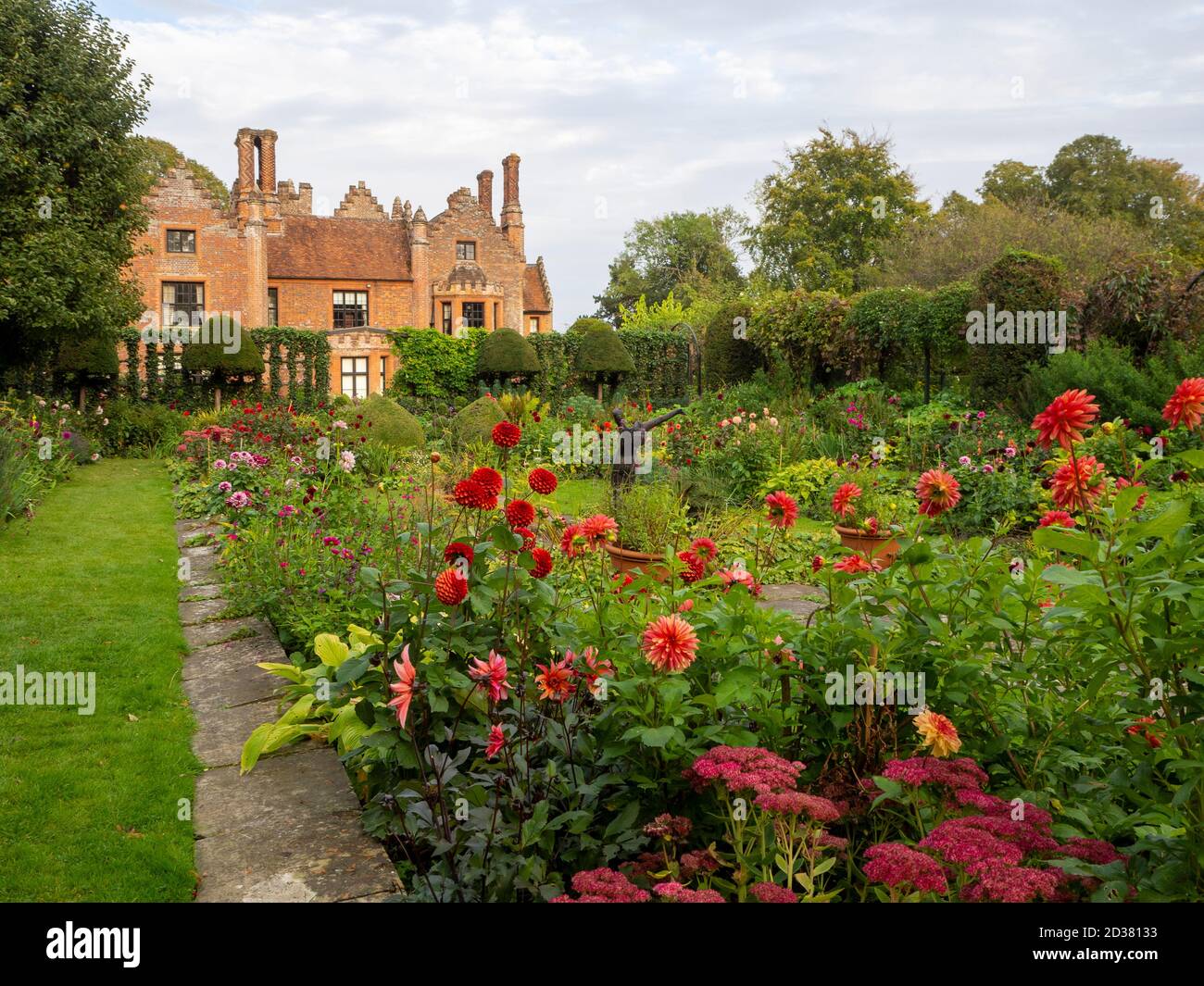 Chenies Manor House au soleil ; le jardin en contrebas en septembre avec la sculpture d'Alan Bigg sur « le plongeur », qui se retrouve à travers l'exposition dynamique des dahlia. Banque D'Images
