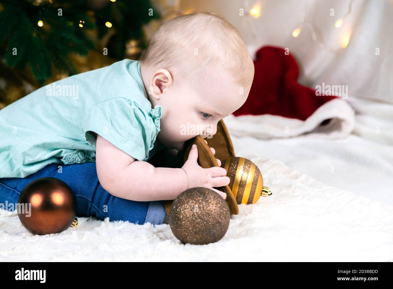 Bébé en jeans et chaussures se trouve près d'un arbre de Noël, des balles  de jouets se trouvent autour. L'enfant joue avec sa jambe Photo Stock -  Alamy