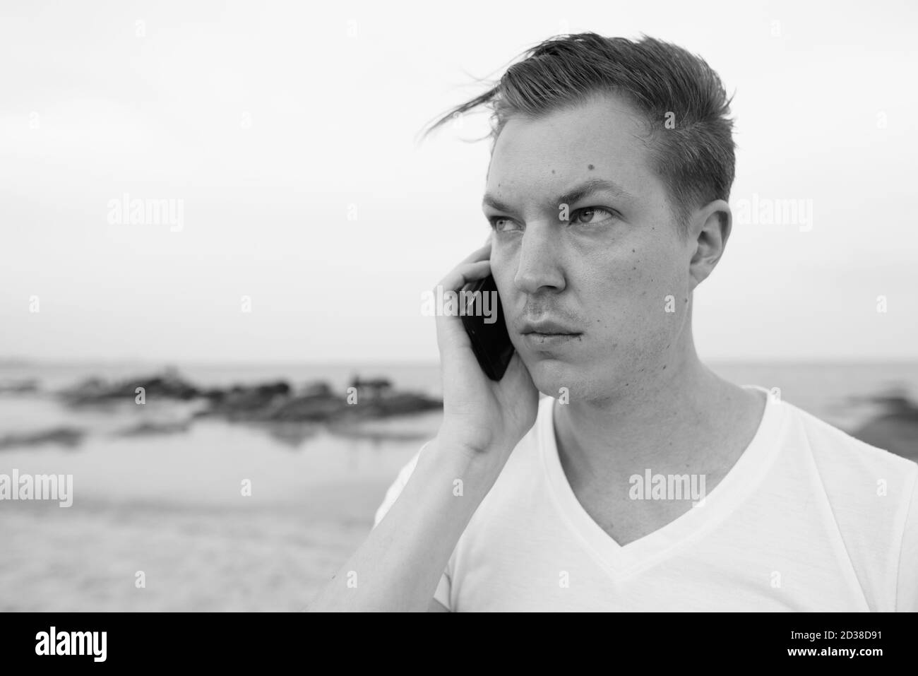 Close up of young man thinking while talking on mobile phone à la plage publique de Hua Hin en Thaïlande Banque D'Images