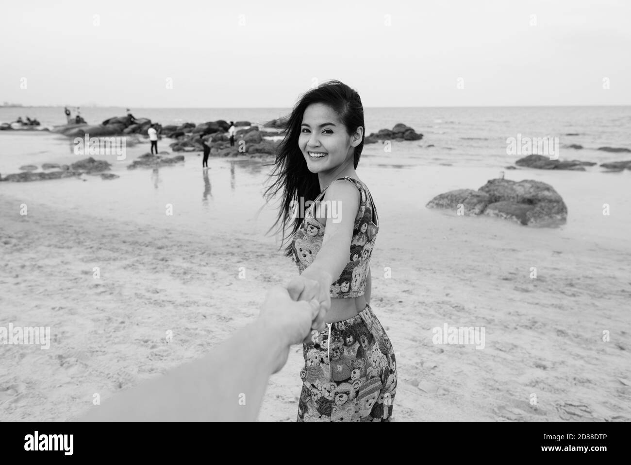 Young happy Asian woman smiling while holding hands and leading man à la plage publique de Hua Hin en Thaïlande Banque D'Images