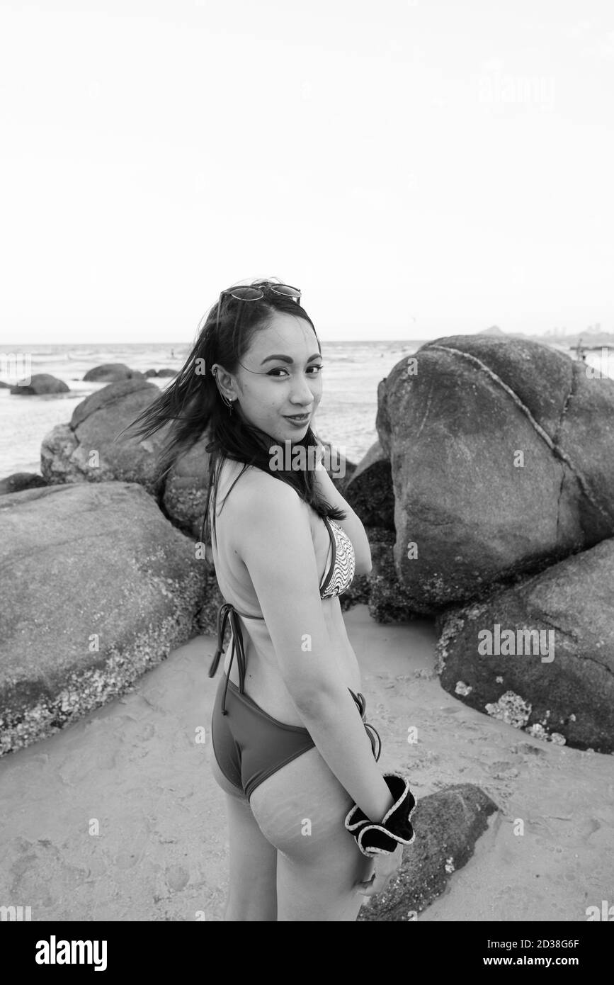 Jeune belle femme asiatique regardant en arrière tout en tenant ses cheveux Et se tenant près des rochers de la plage publique à Hua Hin Thaïlande Banque D'Images