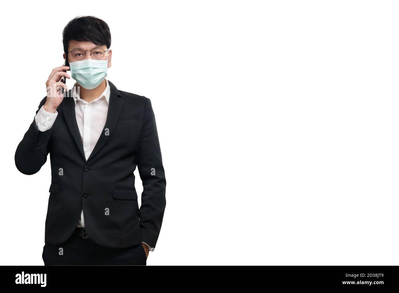 Homme d'affaires asiatique portant un masque chirurgical dans une veste de costume classique noire, en utilisant un smartphone pour parler à la main droite, regardez l'appareil photo, lumière studio Banque D'Images