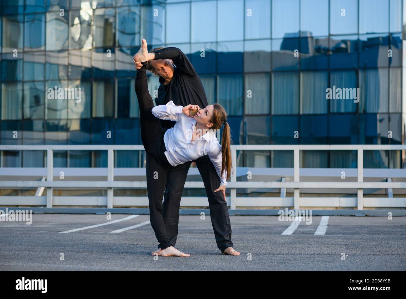 Flexible femme faire l'élément de yoga acro, s'étendant avec le partenaire de base masculin tout en parler par téléphone mobile en milieu urbain, le sport et les affaires Banque D'Images