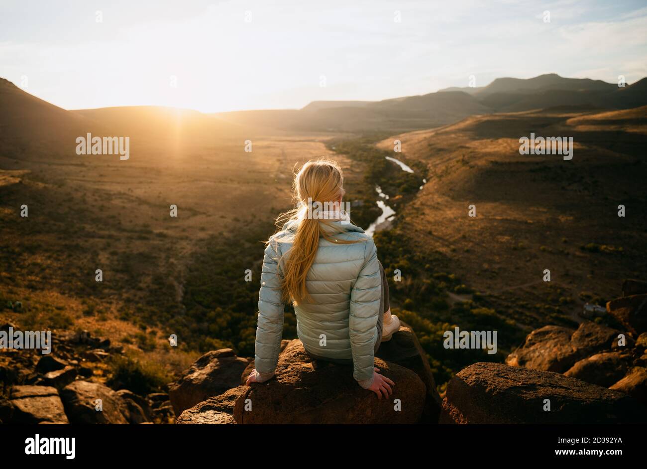 Femme caucasienne assise sur un rocher au sommet d'une montagne en admirant le coucher de soleil après une randonnée, vue incroyable Banque D'Images