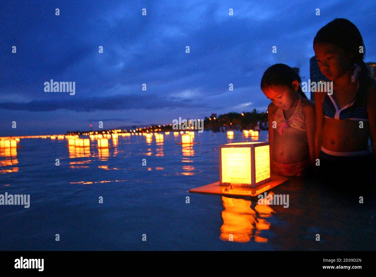 Two girls watch one of about a thousand lanterns set afloat in the waters  off of Ala Moana Beach near Waikiki in Honolulu, Hawaii. Two girls watch  one of about a thousand