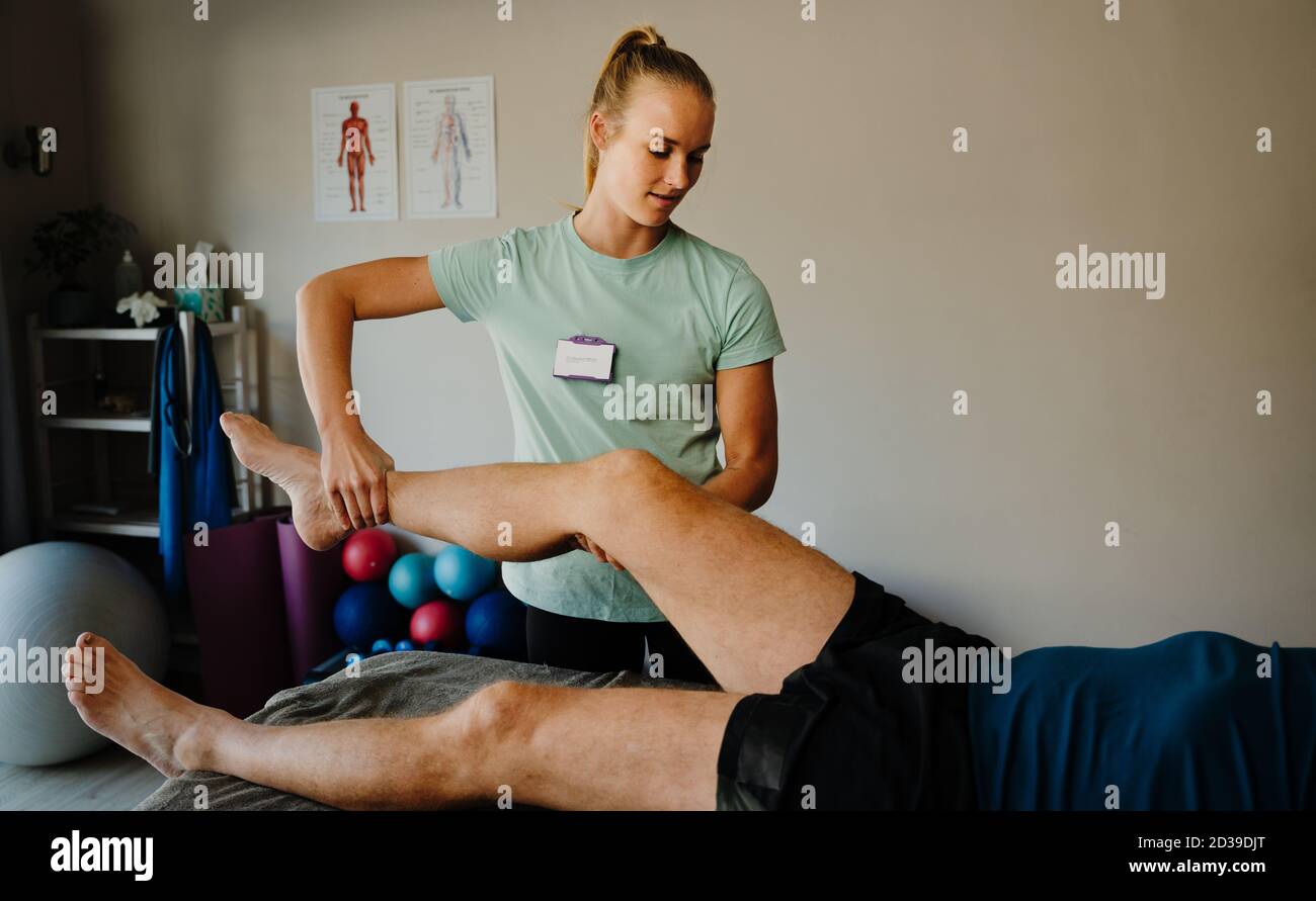 Physiothérapeute femme examinant la jambe de son premier patient mâle couché sur un lit pliant dans la salle de conditionnement physique Banque D'Images