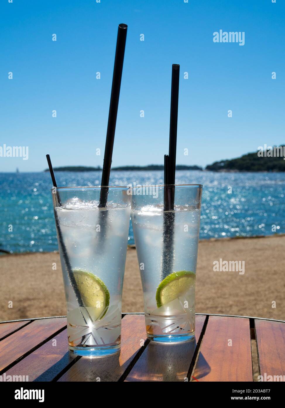 Deux verres de gin tonique avec pailles noires sur un bureau en bois. Mer sur fond flou. Banque D'Images