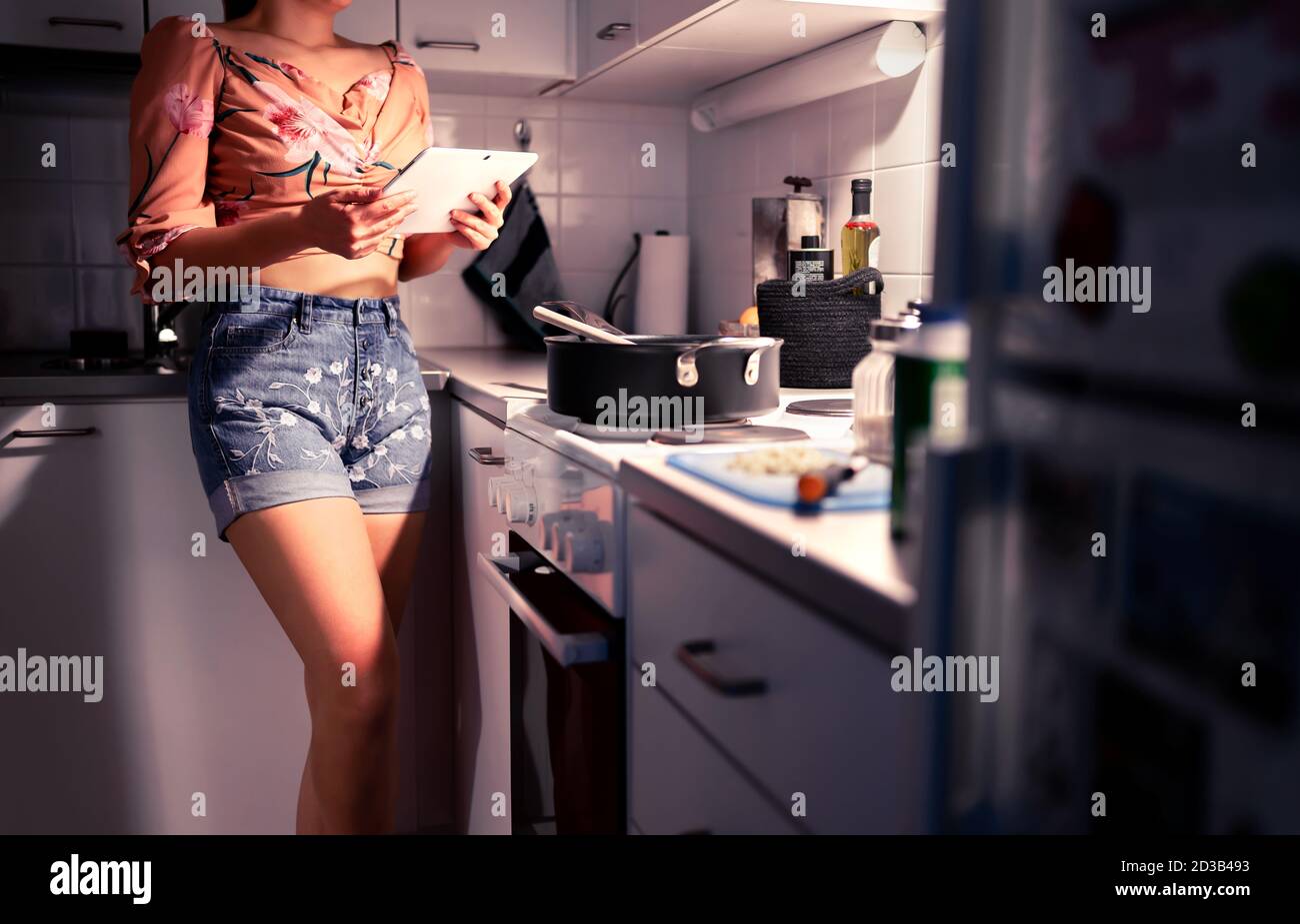 Femme cuisinant et utilisant une tablette dans la cuisine. Recette en ligne pour le dîner. Classe de chef Internet. Étudiant lisant un site Web et apprenant à cuisiner. Banque D'Images