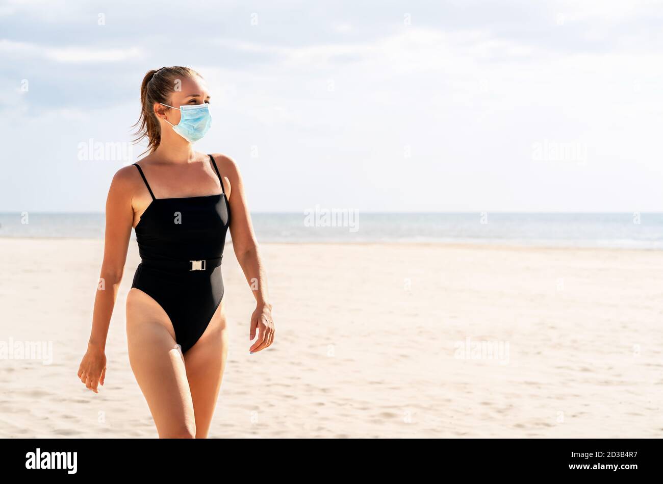 Jolie femme avec un masque sur la plage. Virus Corona et concept de vacances d'été. Modèle portant un masque facial et un maillot de bain. Destination de vacances tropicale vide. Banque D'Images