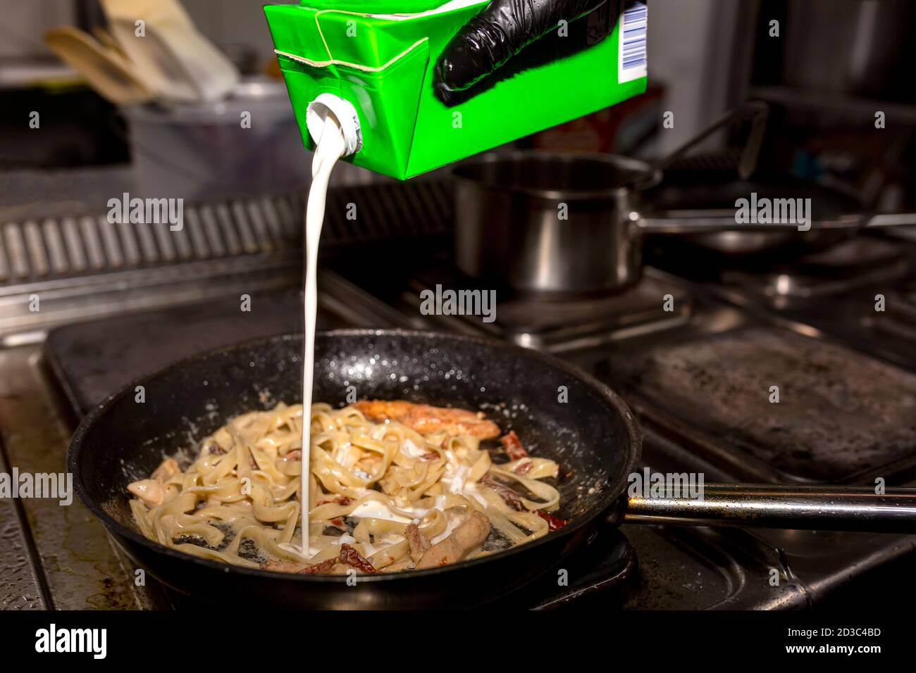 Le cuisinier ajoute de la crème aux pâtes qu'il réchauffe dans une casserole noire Banque D'Images