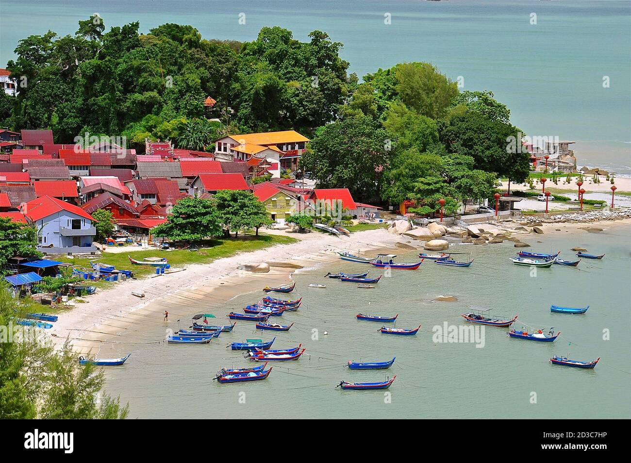 Un village de pêcheurs en Asie avec des toits de tuiles rouges et des bateaux de pêche colorés amarrés dans un port calme. Banque D'Images