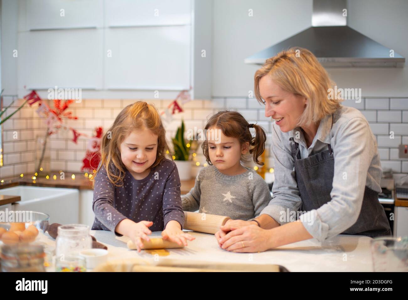 Une femme blonde portant un tablier bleu et deux filles debout dans la cuisine, cuisant des biscuits de Noël. Banque D'Images