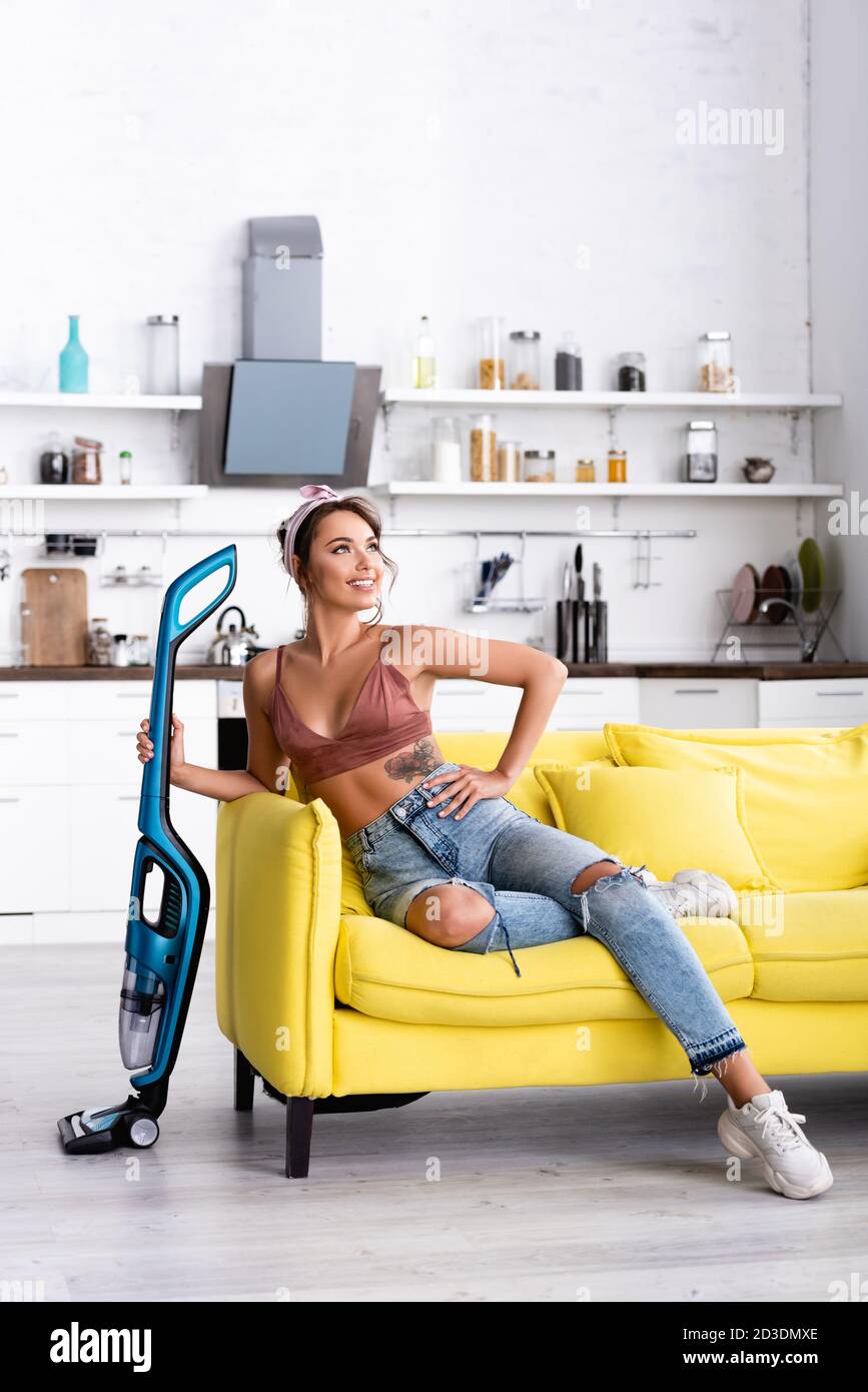 Femme au foyer avec la main sur la hanche regardant loin et tenant le vide nettoyant Banque D'Images